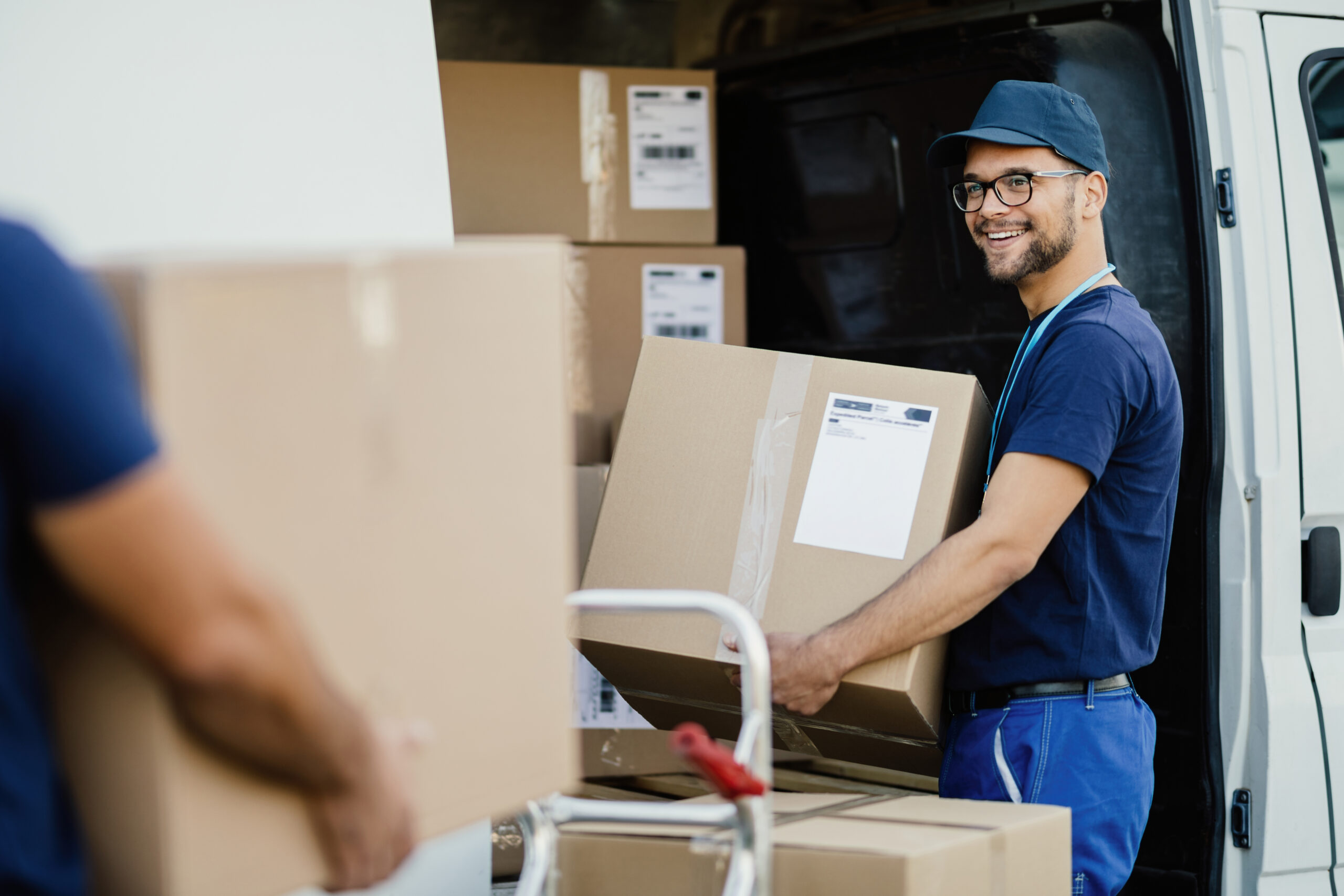 happy delivery man talking with coworker while loading boxes in